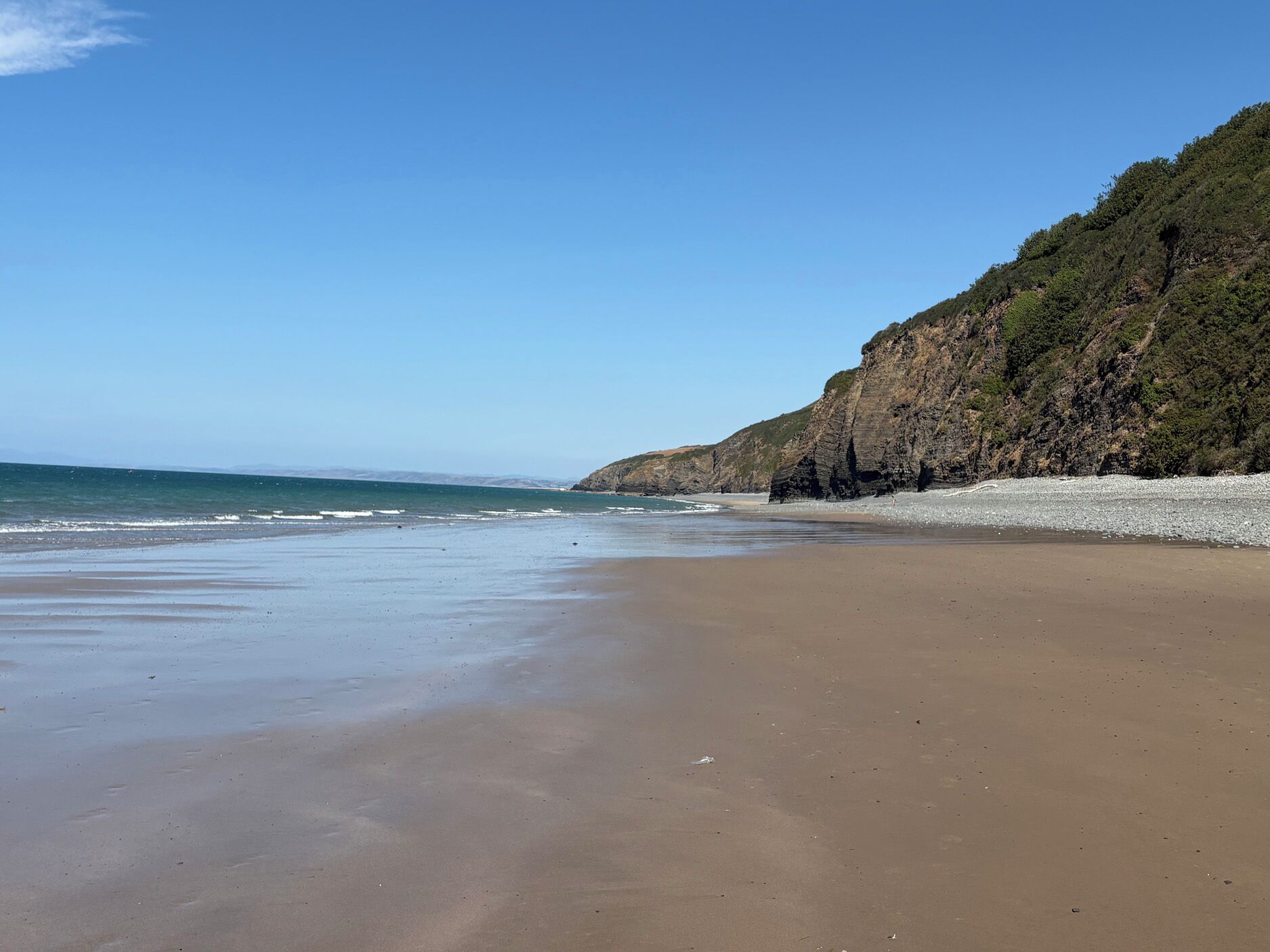 A beach with a clear sky, a sandy shore, and a rocky cliff.