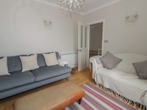 Una sala de estar con un sofá gris, un sillón blanco, un tapete a rayas y un banco de madera.