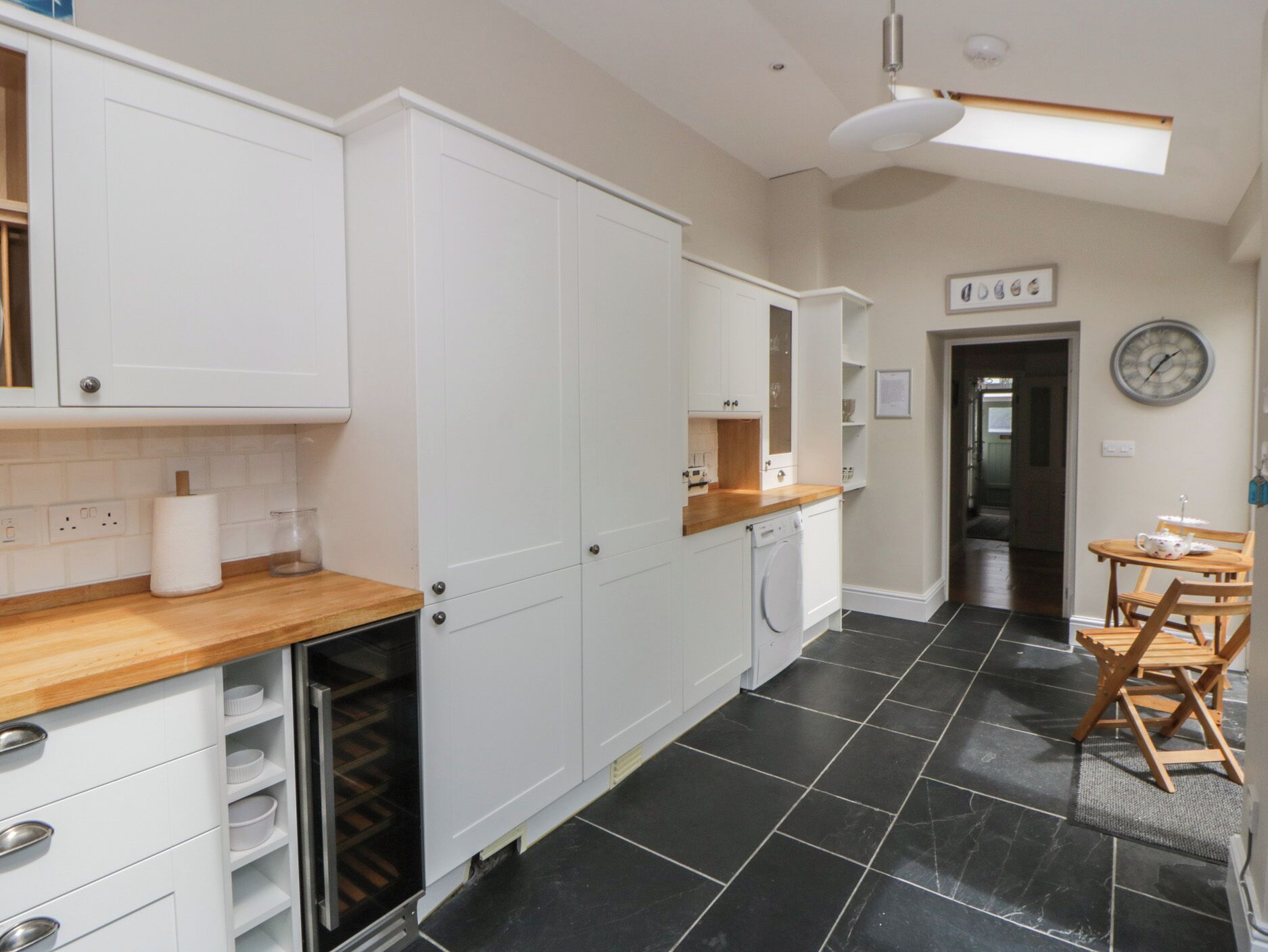 A kitchen with white cabinets, a wooden countertop, a black tiled floor, and a dining area with a table and chairs.