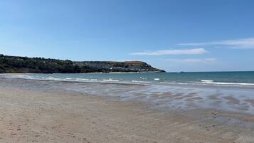 A beach with a clear sky, calm sea, and a distant town.