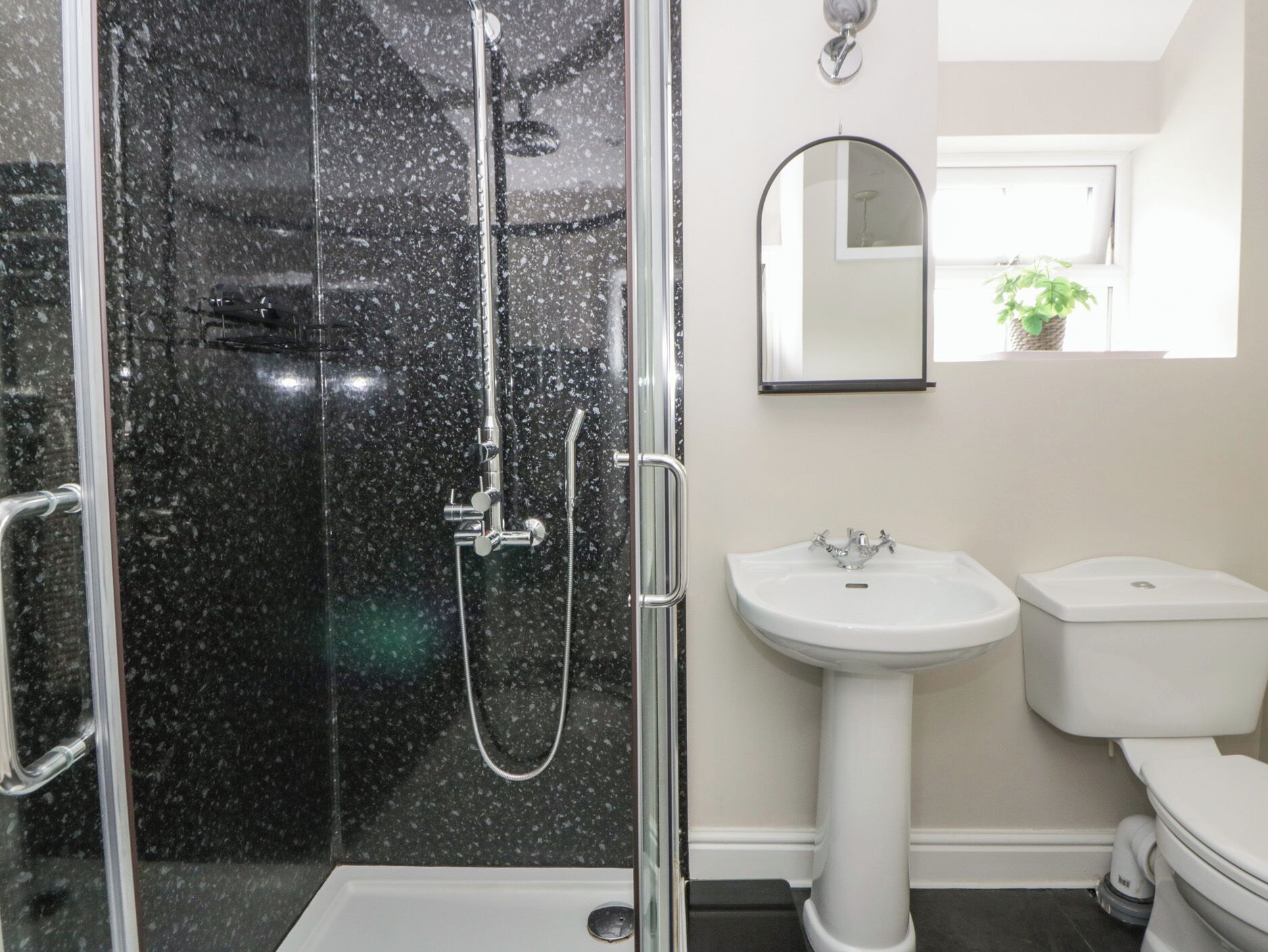 Une salle de bain avec une douche à parois de verre, un lavabo sur colonne blanc et des toilettes.