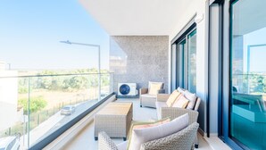 Ein Balkon mit Korbmöbeln, ein großes Fenster und Blick auf eine Straße.