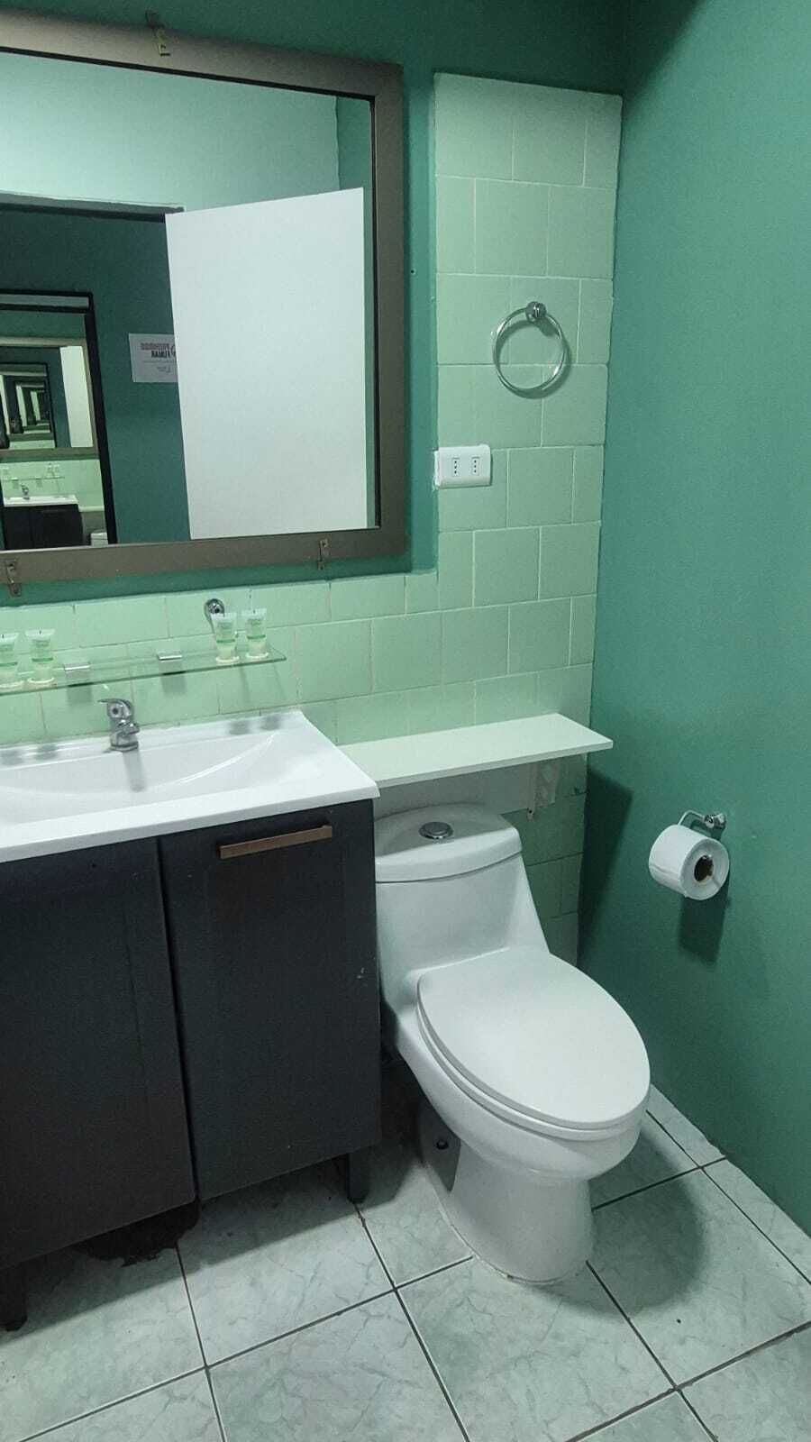 A bathroom with a white sink, dark cabinet, white toilet, and green walls.