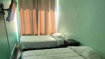 A room with two beds, a window with curtains, and a wall-mounted light fixture.