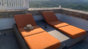 Terraza en la azotea con dos sillones naranjas, un sofá de fibras naturales y vistas a montañas distantes.