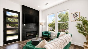 A living room with a black fireplace, green sofa, and large windows. - Welcome to The Hollywood House, a glamorous 5 bedroom, 4 bathroom escape in the aptly named Dallas Hollywood neighborhood. (Dallas)