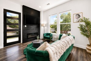 A living room with a black fireplace, green sofa, and large windows.