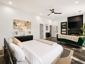 A modern bedroom with a large bed, a TV, a fireplace, and a ceiling fan.