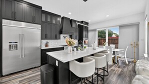 A modern kitchen with stainless steel appliances, a central island with bar stools, and a dining area with a white table and chairs. - Welcome to The Hollywood House, a glamorous 5 bedroom, 4 bathroom escape in the aptly named Dallas Hollywood neighborhood. (Dallas)