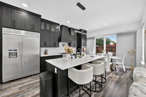 A modern kitchen with stainless steel appliances, a central island with bar stools, and a dining area with a white table and chairs.