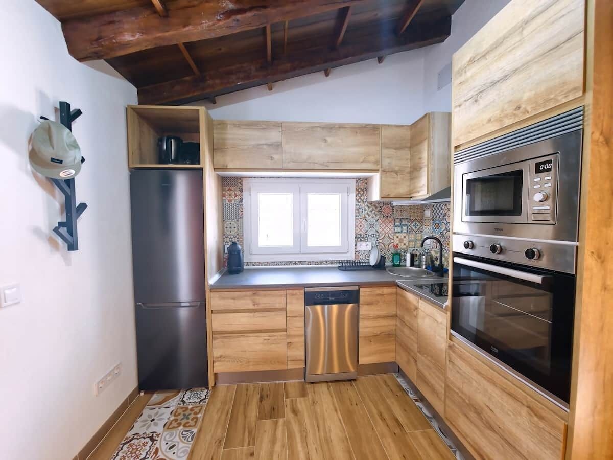 A compact kitchen with wooden cabinets, a stainless steel refrigerator, a dishwasher, a microwave, and an oven.