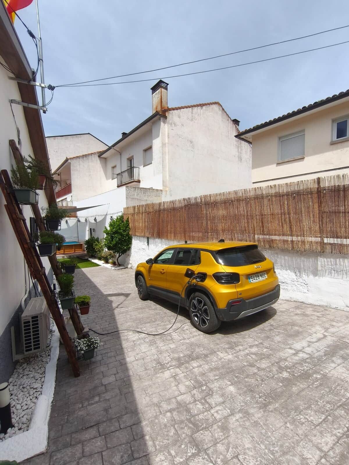 Un SUV amarillo estacionado en una entrada con un muro blanco y una cerca de madera al fondo.