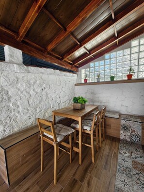A wooden dining table with chairs, a stone wall, and a window with potted plants.