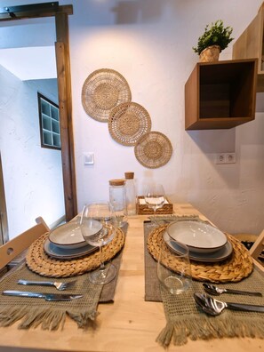 A dining table set with plates, cutlery, and glassware, accompanied by woven placemats and a wall-mounted decorative item.