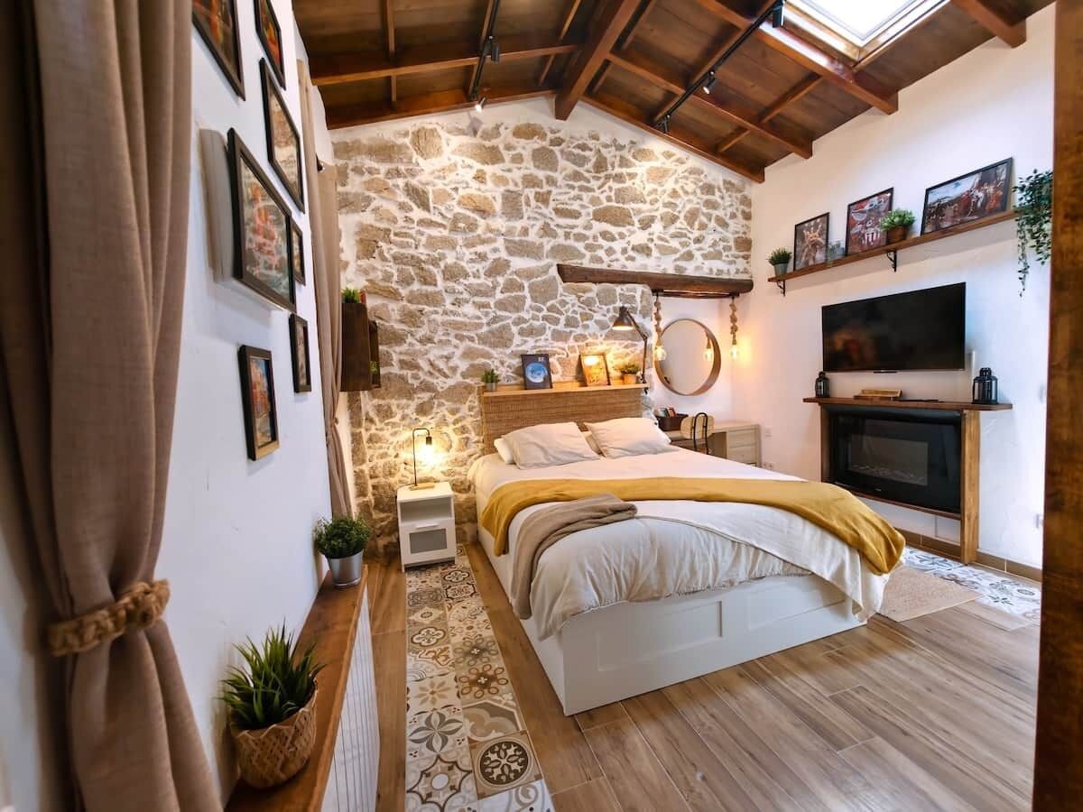 Un dormitorio con pared de piedra, cama, televisor y chimenea.