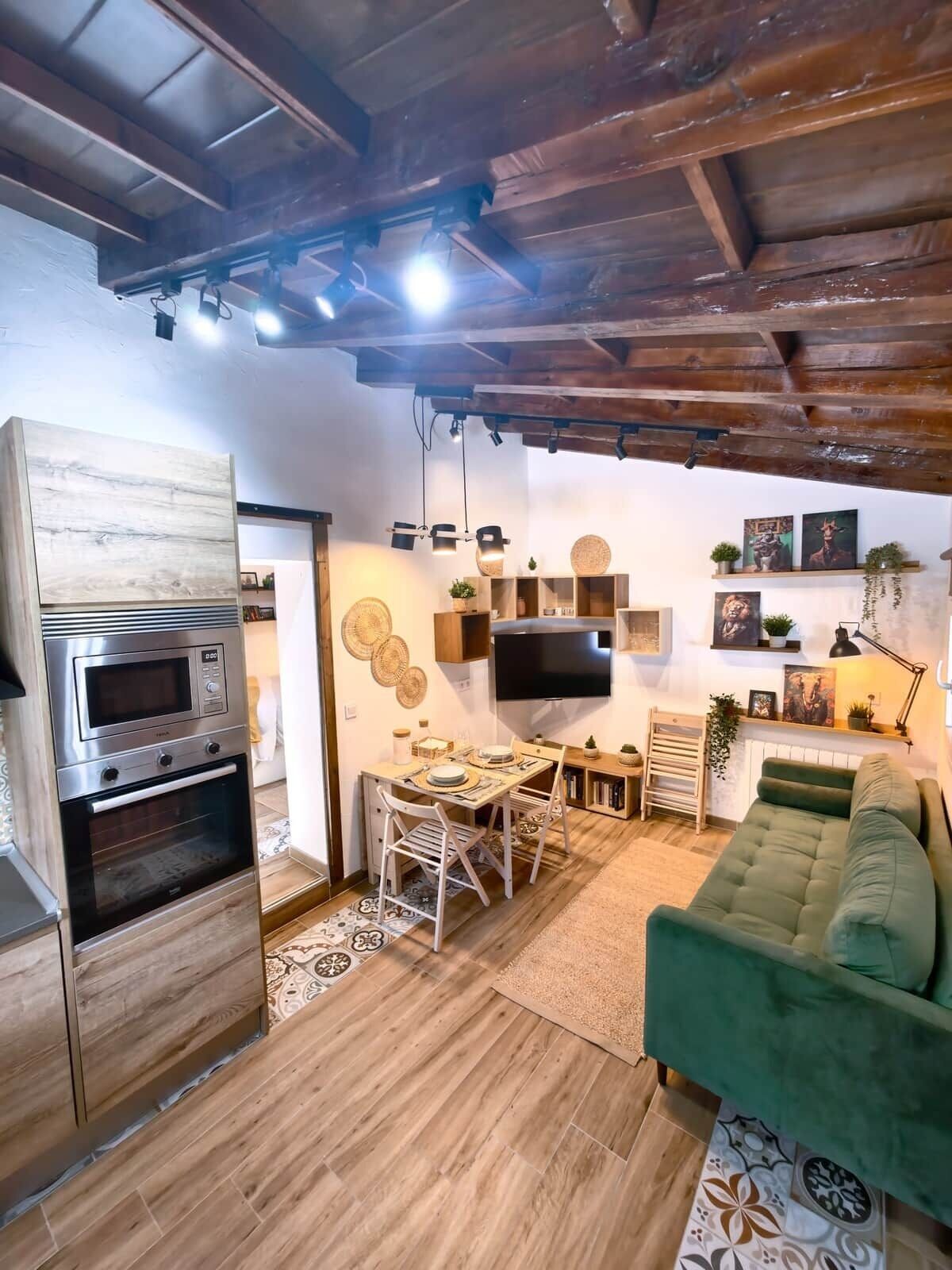 Een moderne keuken met inbouwapparatuur, een eethoek met een houten tafel en stoelen, en een groene bank in een zithoek met een wandgemonteerde flatscreen-tv.