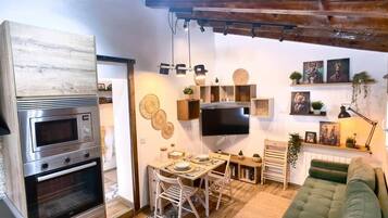 Een moderne keuken met inbouwapparatuur, een eethoek met een houten tafel en stoelen, en een groene bank in een zithoek met een wandgemonteerde flatscreen-tv.