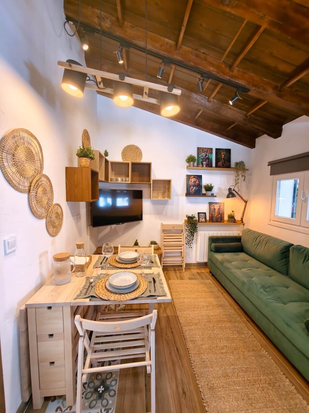 Un espacio de sala acogedor con comedor, un sofá verde y un televisor montado en la pared.