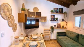 A cozy living space with a dining area, a green sofa, and a television mounted on the wall.
