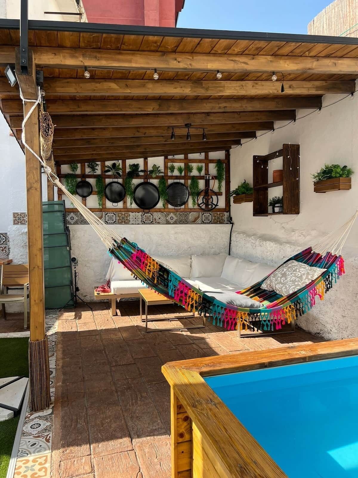 Eine Hängematte unter einer Holzpergola, ein Swimmingpool und eine geflieste Terrassenfläche.