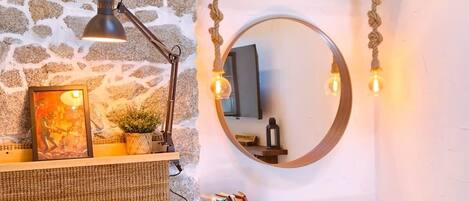 A cozy room with a stone wall, a round mirror, a desk with a basket, and a bed with a pillow.