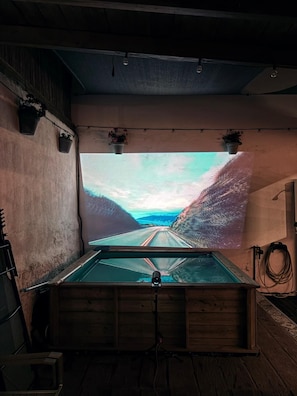 A room with a large projection screen displaying a scenic road view, wooden walls, and a wooden floor.