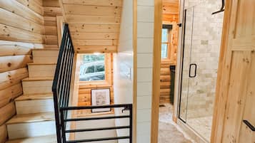 Un intérieur en bois avec un escalier, une porte en verre donnant sur une salle de bain et une vue sur l’extérieur.