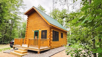 Une cabane en rondins avec une véranda, une porte verte et des fenêtres.