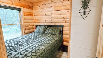 Quarto de cabana de madeira com uma cama, um ventilador de teto, uma janela e uma planta fixada na parede.