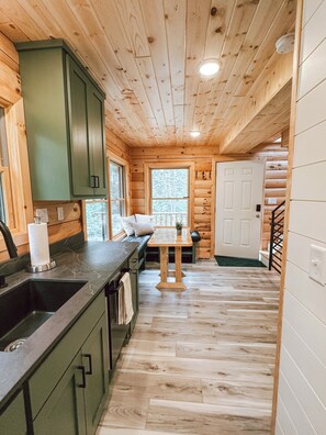 Interior de una cabaña de madera con cocina, una mesa de comedor y una escalera.