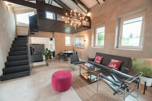 Ein modernes Interieur mit Treppe, Essbereich, einer Couch mit roten Kissen und einer Pendelleuchte.