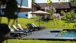 Ein Poolbereich mit Liegestühlen und Sonnenschirmen, ein kleiner Pool und ein Gebäude mit einem Ziegeldach.