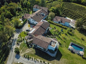 An aerial view of a residential area with multiple houses, a swimming pool, and a vineyard. - Pool house 5 mins from town among vineyards (Novello)