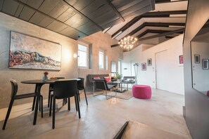 Ein geräumiges Zimmer mit Essbereich, einer Couch, einem roten Hocker und einem großen abstrakten Gemälde an der Wand.