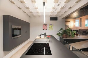 A modern kitchen with a built-in oven, a central island with a stovetop, and a dining area with chairs and a table. - Pool house 5 mins from town among vineyards (Novello)