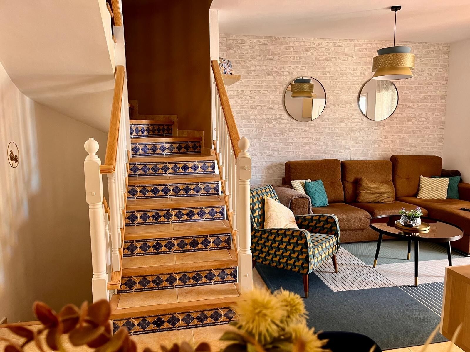 Una escalera con baldosas estampadas, un sofá marrón, un sillón con estampado y un espejo redondo en la pared.