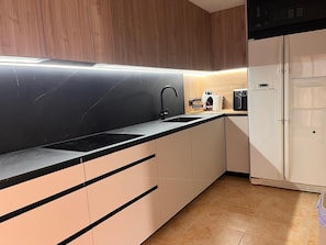 Eine moderne Küche mit schwarzem Arbeitsplatz, einem Spülbecken, einer Kaffeemaschine und einem weißen Kühlschrank.