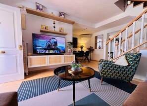 Ein Wohnzimmer mit Fernseher, Sofa, Couchtisch und einer Treppe.