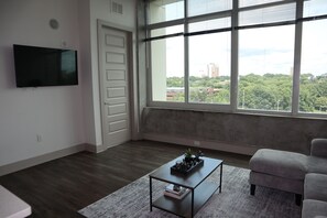 A room with a large window, a flat-screen TV, a coffee table with books, and a gray sofa. - Relax, Recharge, Explore. Where Luxury Meets Comfort l The Perfect Atlanta Stay (Atlanta)