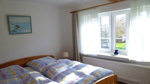 Un dormitorio con una cama, una ventana con cortinas, un radiador y un cuadro en la pared.