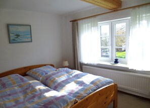 A bedroom with a bed, a window with curtains, a radiator, and a painting on the wall. - Living under a thatched roof, in the quiet neighborhood of Fahretoft, 8 km from the North Sea (Dagebüll)