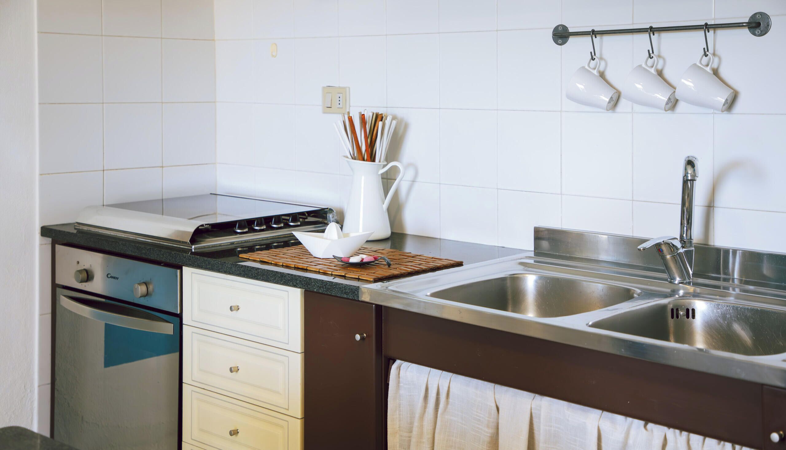 Uma cozinha com fogão, forno, pia e suporte para utensílios pendurado.