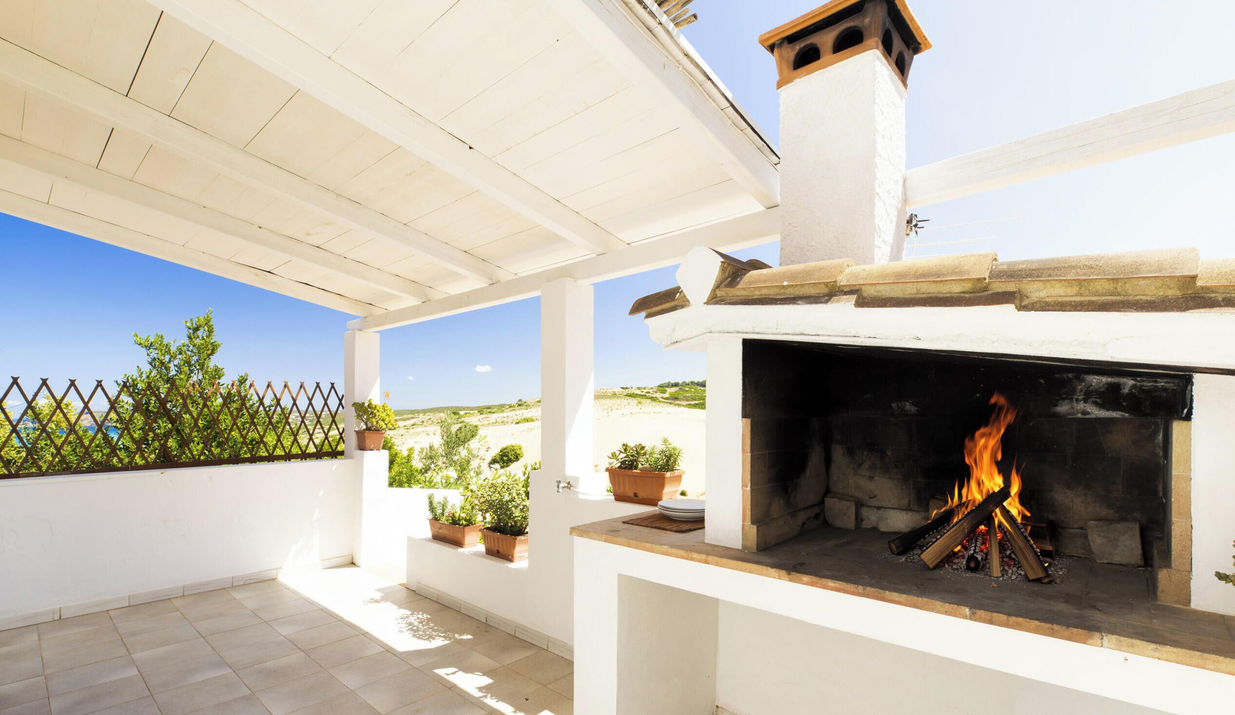 A covered outdoor area with a fireplace, potted plants, and a view of the landscape.
