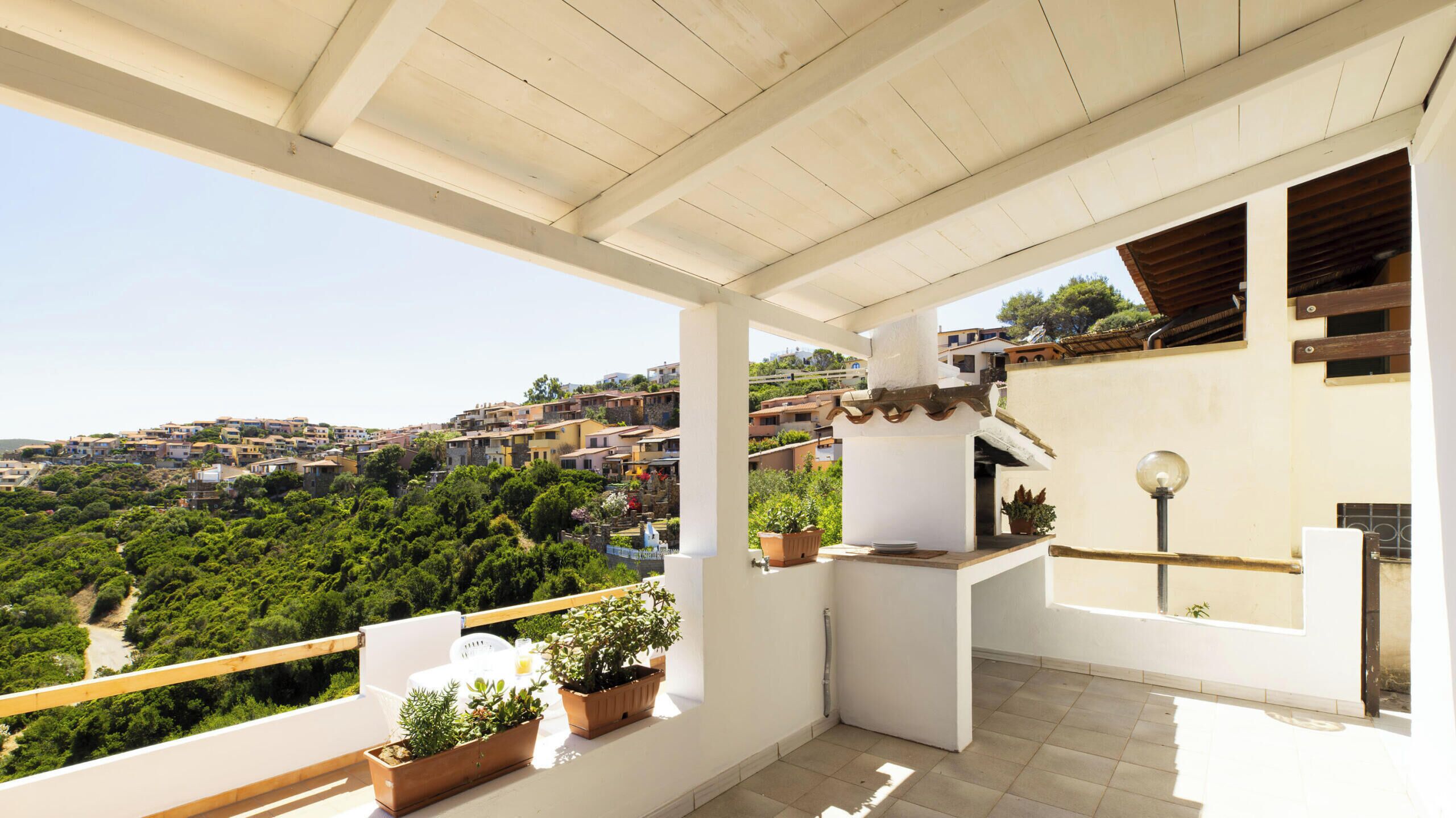 A balcony with potted plants, a table, and a view of a hillside town.