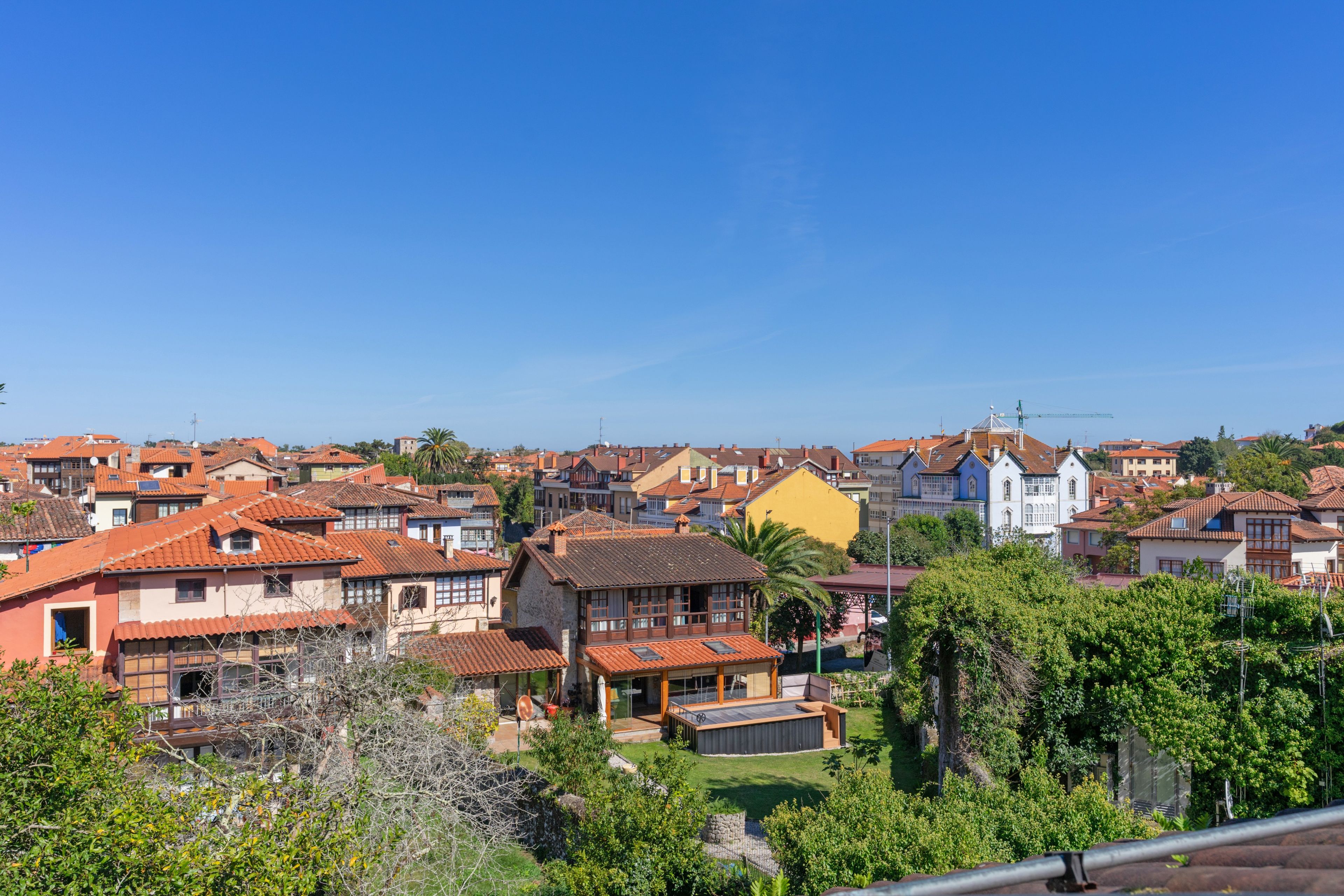 Un barrio residencial con una mezcla de casas tradicionales y modernas, algunas con techos de tejas rojas, y un cielo azul despejado.