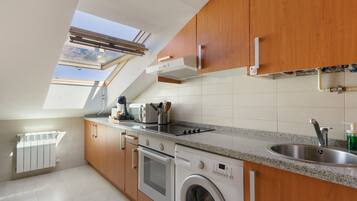 A modern kitchen with wooden cabinets, a built-in oven, a washing machine, and a skylight.