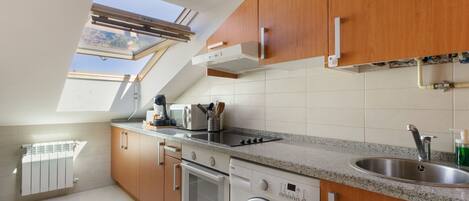 A modern kitchen with wooden cabinets, a built-in oven, a washing machine, and a skylight.