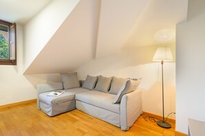 Habitación de esquina con sofá seccional de color gris claro, una lámpara de pie y suelo de madera.