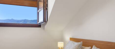 A bedroom with a bed, a nightstand with a lamp, and a window offering a mountain view.