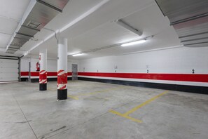 Un estacionamiento con paredes blancas, franjas rojas y negras, espacios numerados y líneas amarillas.